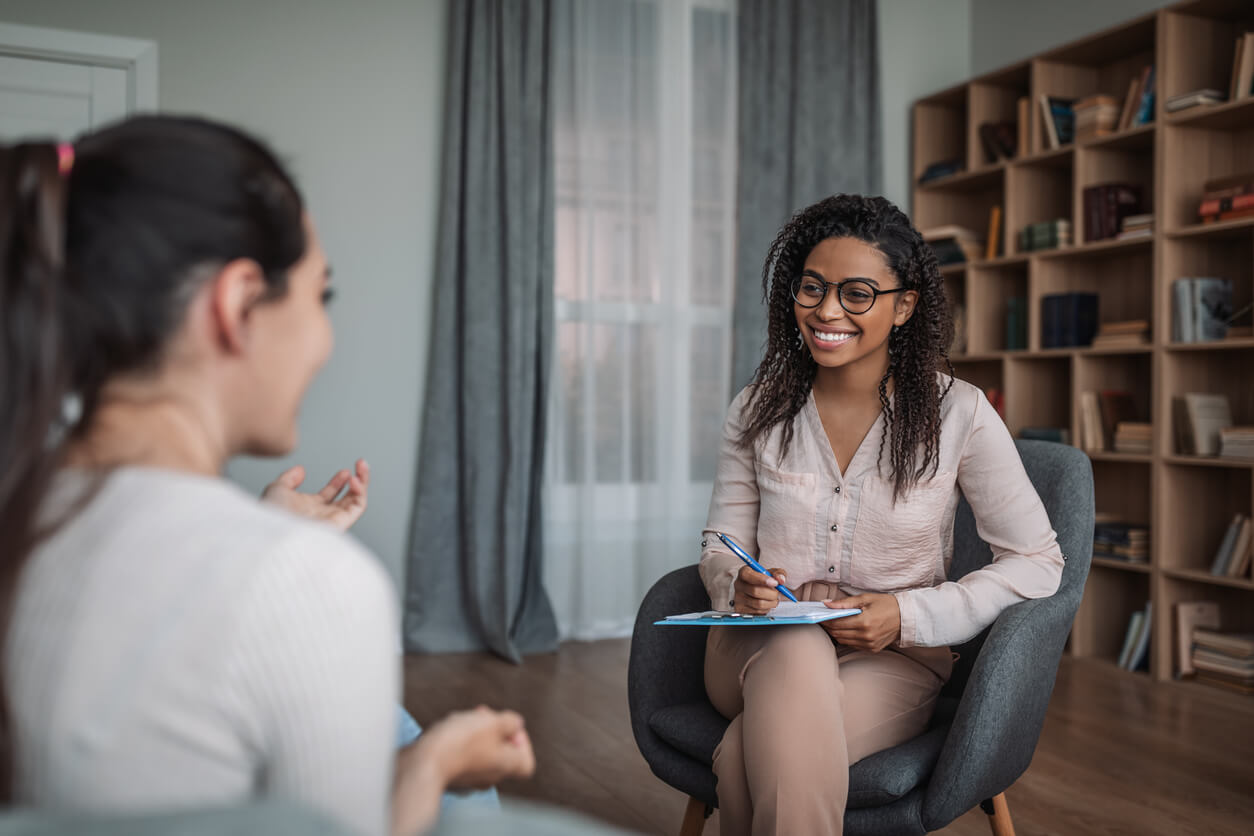 Smiling young black female doctor psychologist consulting european woman in modern mental clinic